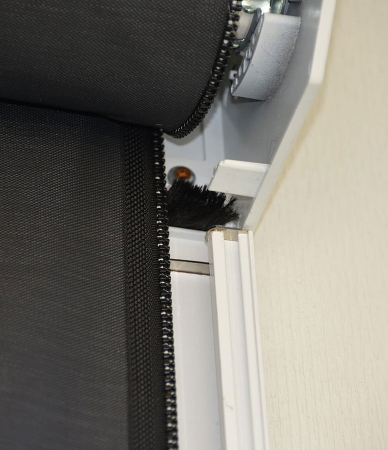 Close-up of the screen roller mechanism showing mesh material, zipper edge, motor assembly, and brush seal at the housing exit point